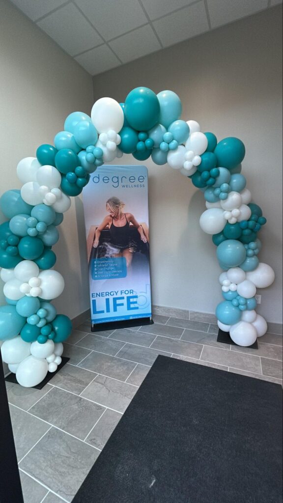 A teal, light blue, and white balloon arch sits in a corner in front of a banner.