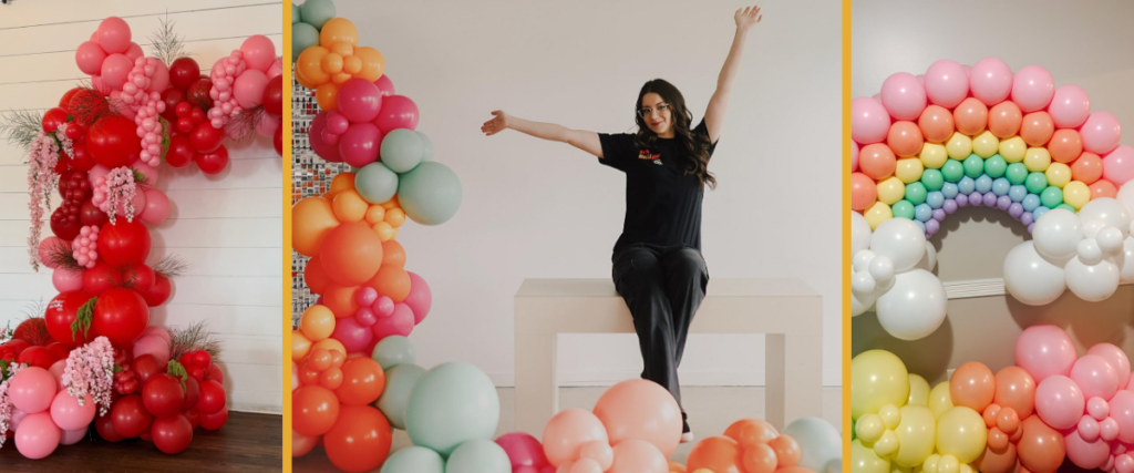 Alexis sits in the middle with her arms up displaying several balloon designs. On the left is a red and pink cascading design of balloons that is reminiscent of flowers and on the right is a rainbow made of balloons.