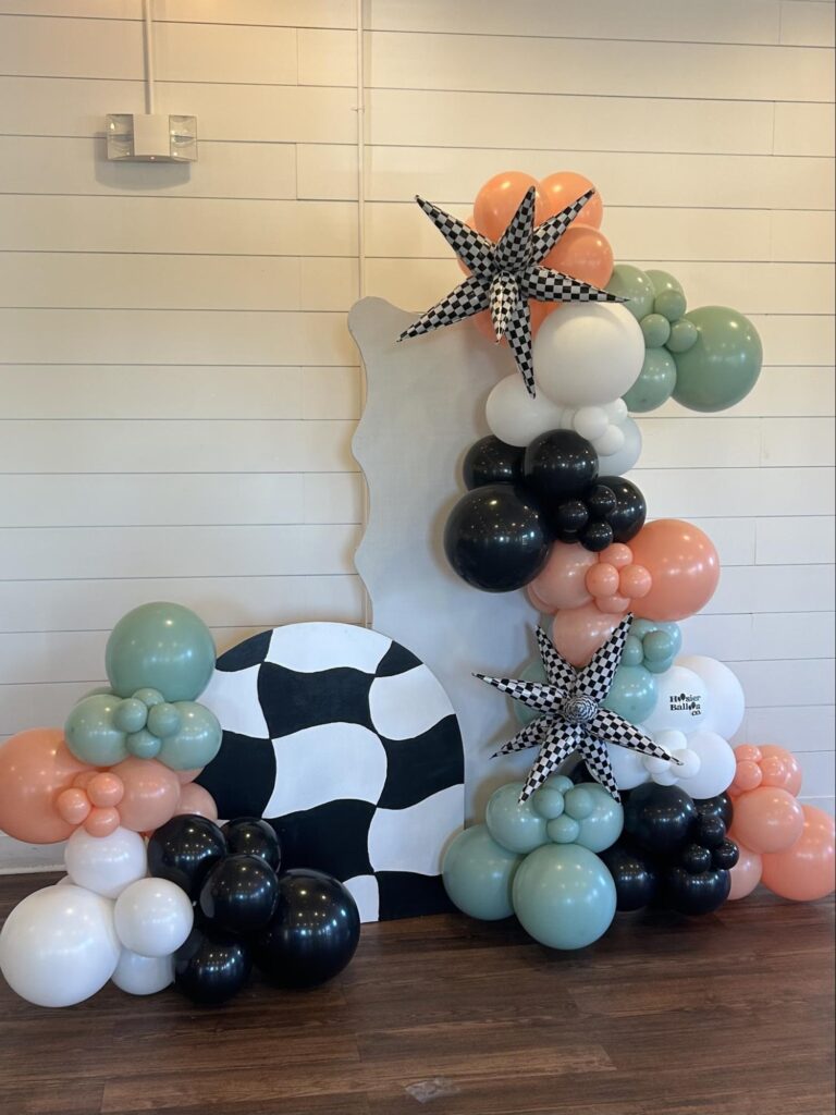 Balloons of white, peach, olive green and black are arranged eloquently around two display boards.