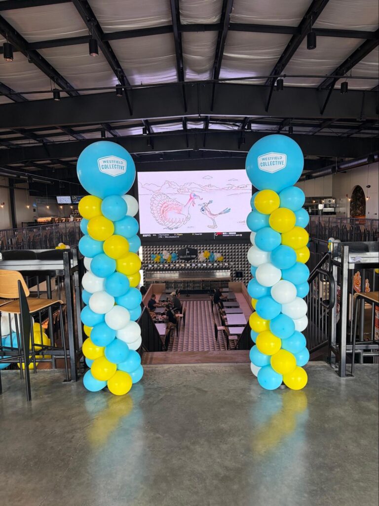 Two turquoise, yellow, and white striped balloon columns create a sort of doorway with a sign in the center.