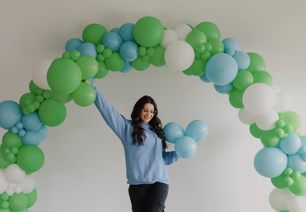 Alexis looks like she's holding up a green, blue and white balloon arch.