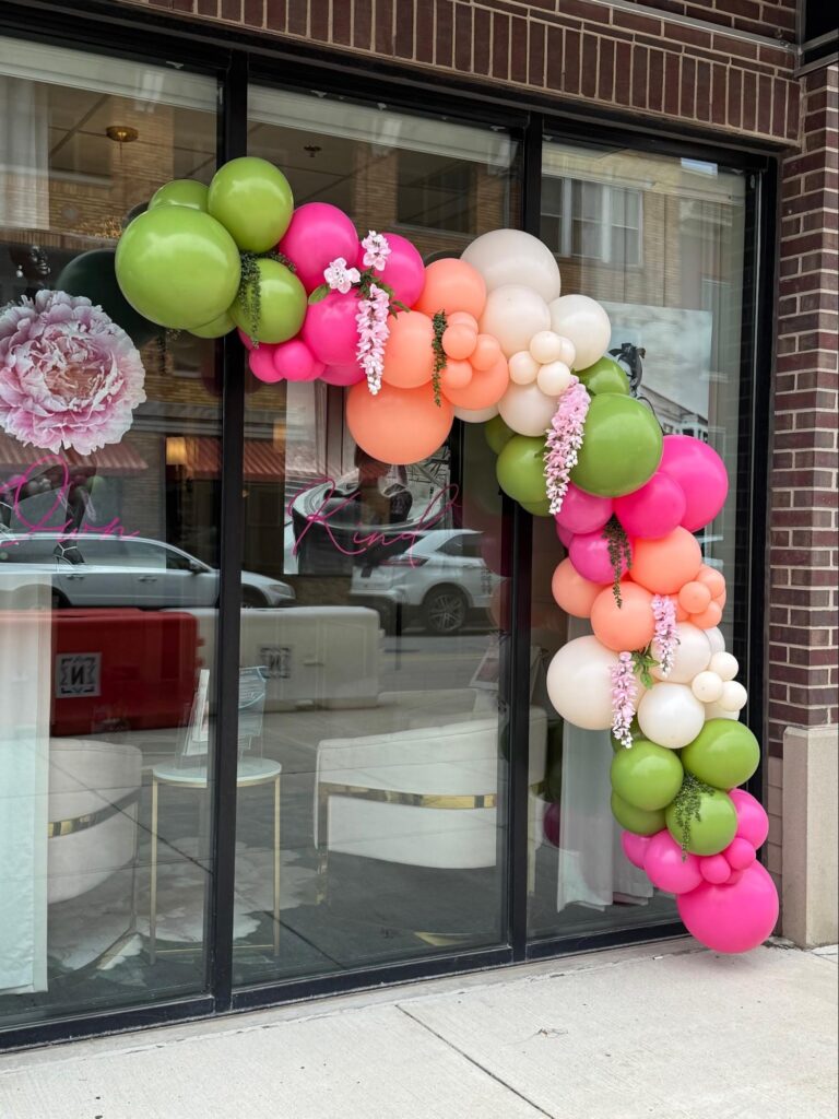 A store front with green, pink, peach, and white balloons cascading down the right-hand side.
