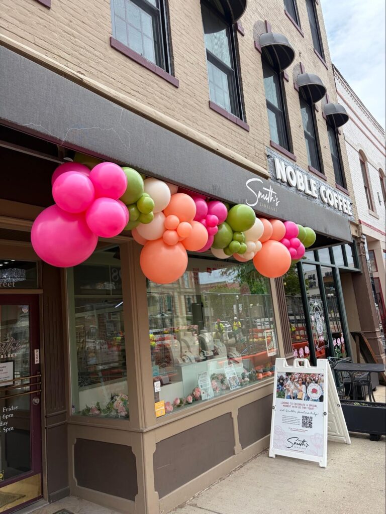 A store front with green, pink, peach, and white balloons hanging from the awning.