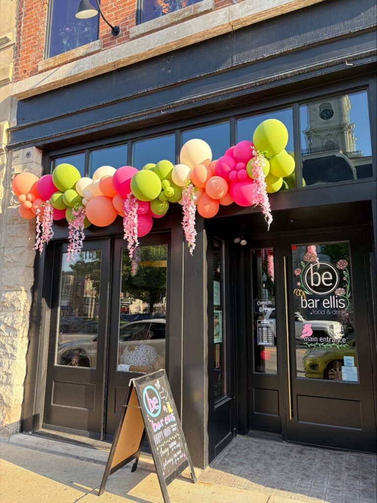 A store front with green, pink, peach, and white balloons attached above the windows and door.