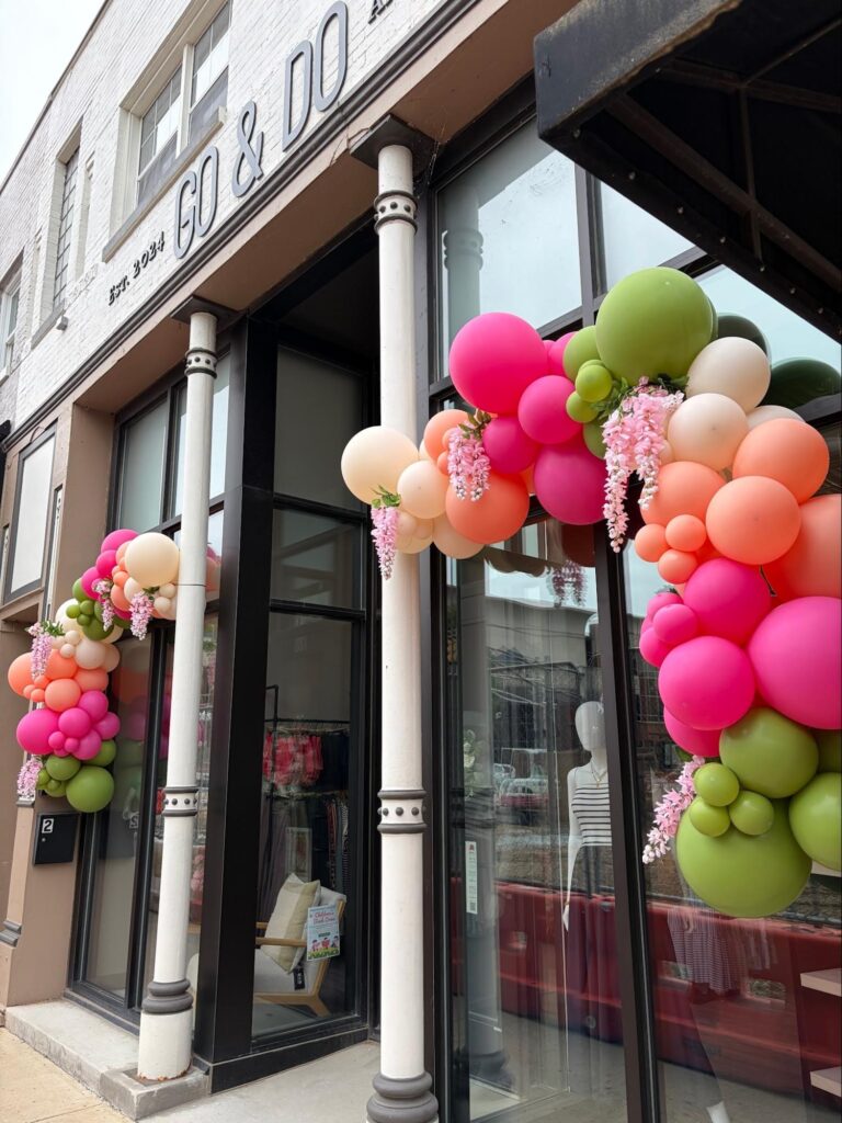 A store front with green, pink, peach, and white balloons cascading down the both sides of the door.