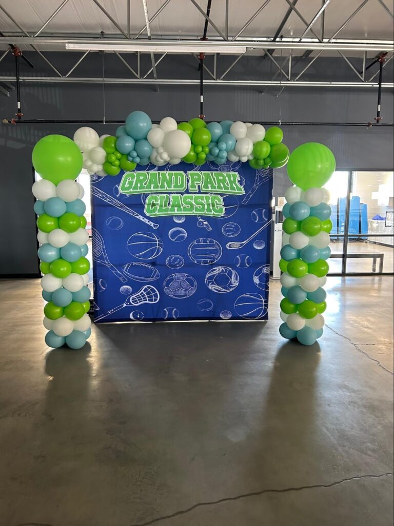 A large blue centerpiece with a balloon arch surrounding it on the left, top and right sides says Grand Park Classic in green letters.